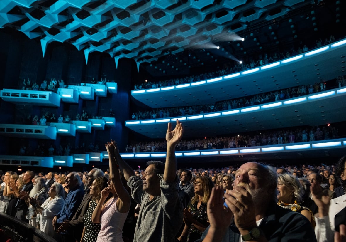 a man raises his hands in the air among a group of people inside of a theatre with blue lights.