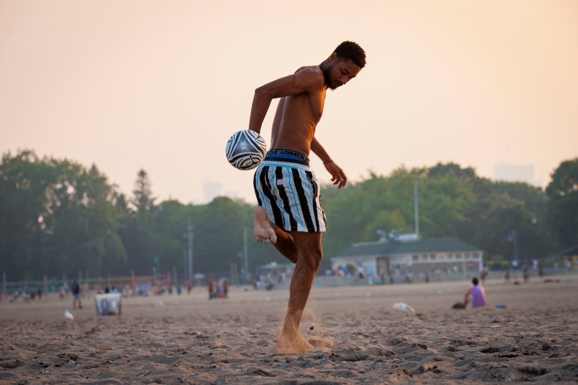 A man wearing a swimsuit kicks a white and black soccer ball while on a sandy beach.