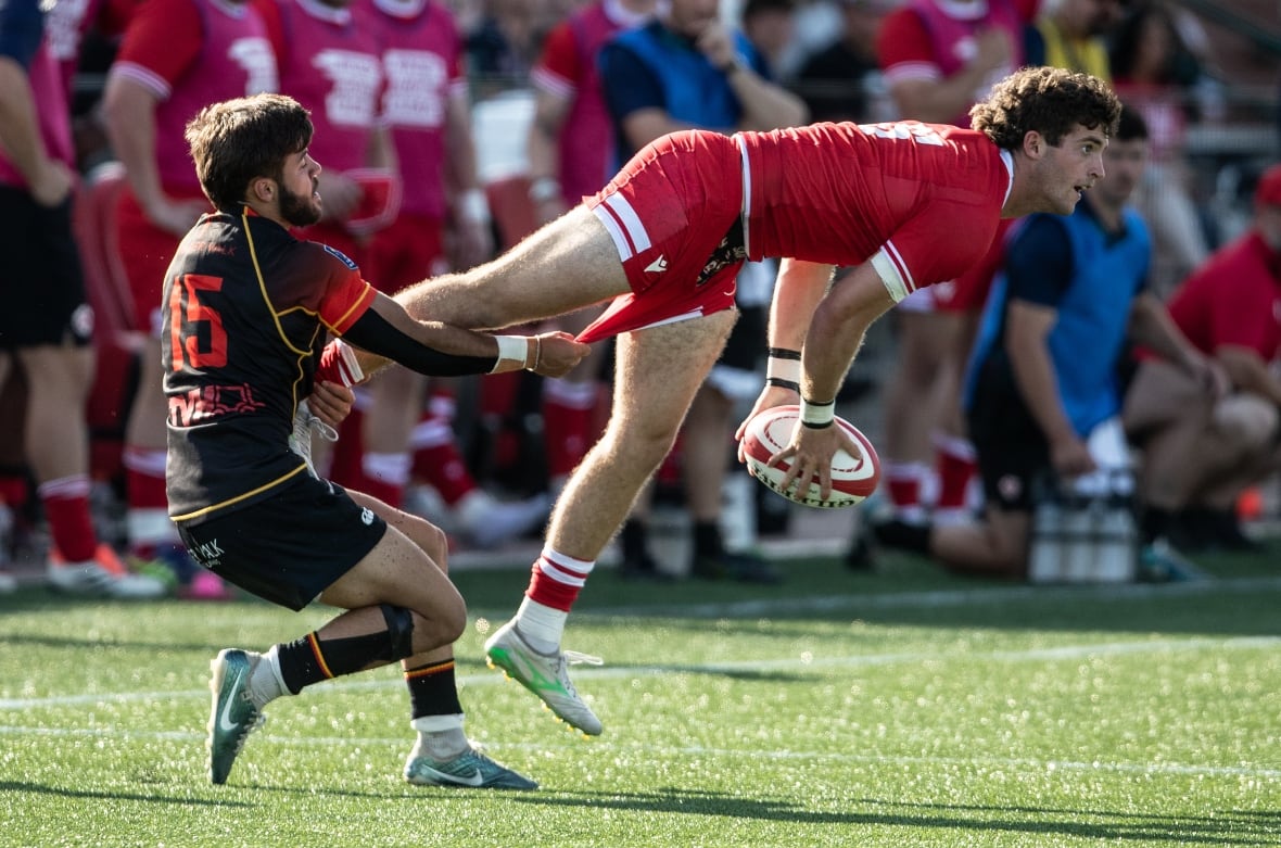 A man jumps in the air wearing a red and white uniform while throwing a white rugby ball while on a sunny field.