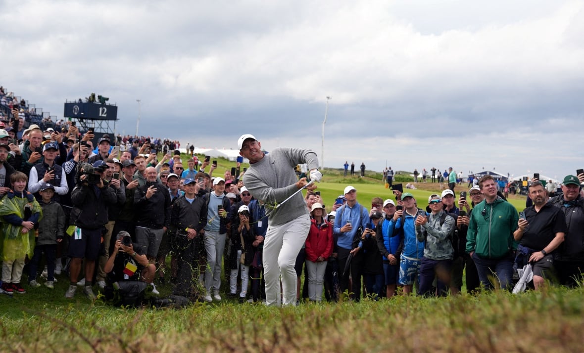 A golfer swings a club while multiple people stand and watch under a cloudy sky.