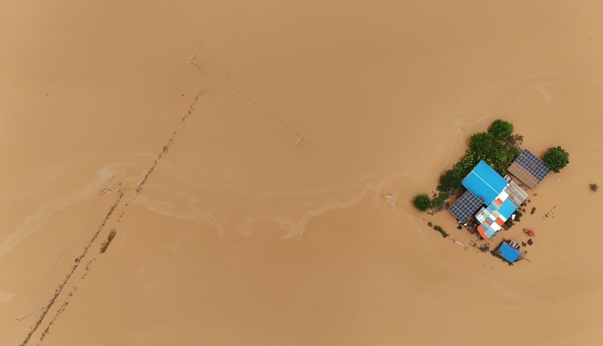 A home with a blue roof is surrounded by brown murky water.
