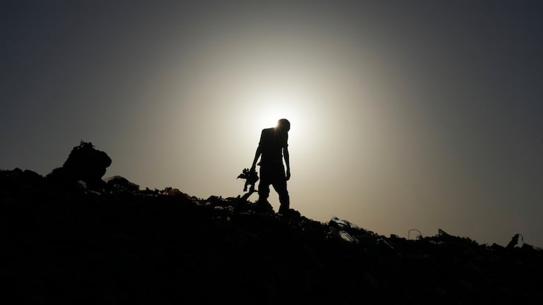 A man walks through debris as the sun sets directly behind him.