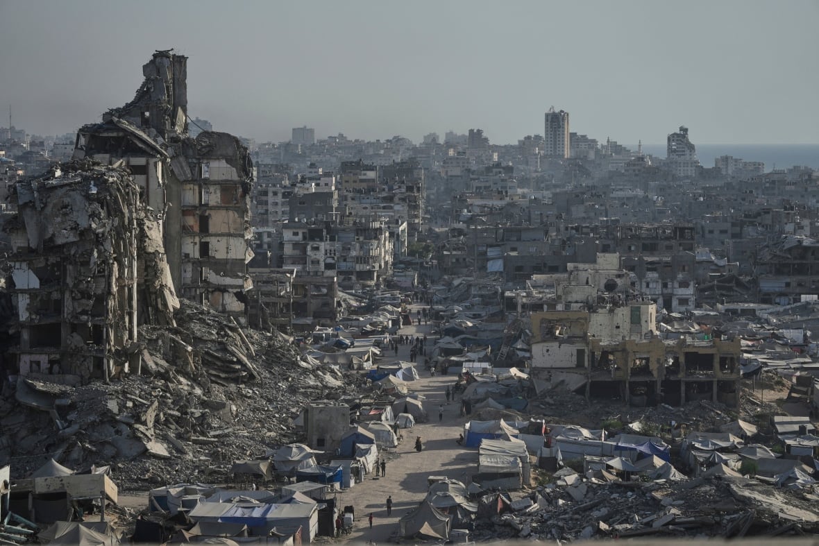 Concrete debris and rubble from destroyed buildings as people walk down a clearing on a street.