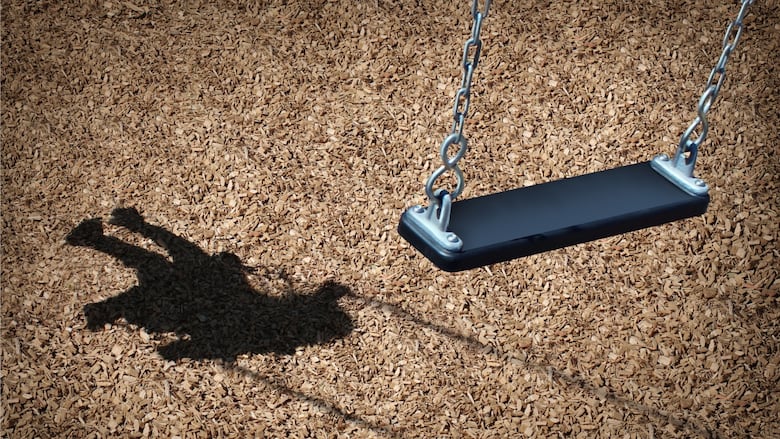 The shadow of a child is seen beside an empty swing in a playground.
