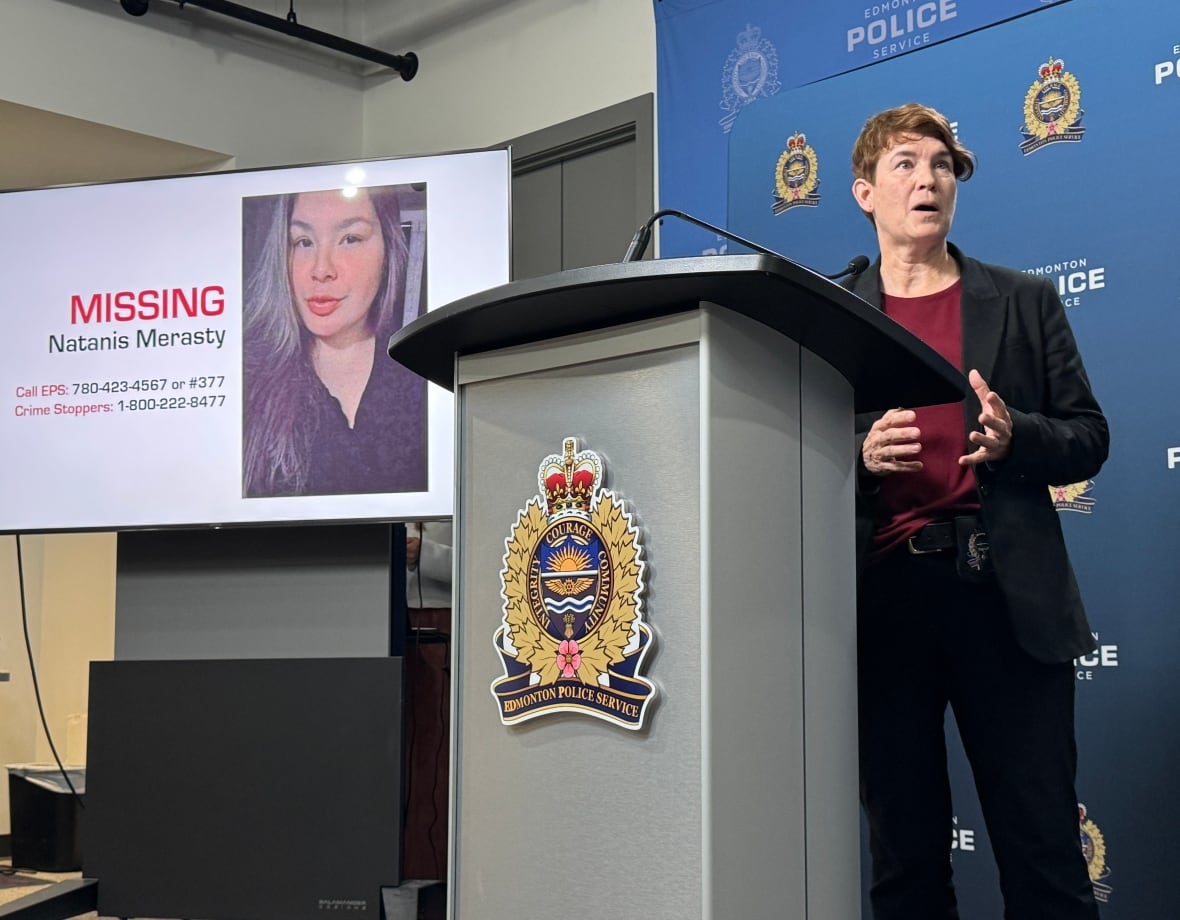 A woman with short hair stands at a podium with an Edmonton police logo, with a woman's face on a screen behind her.