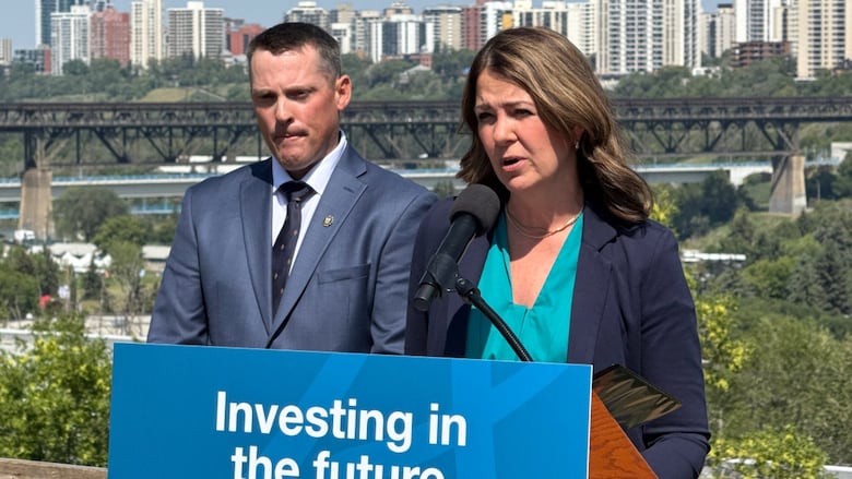 Two people at a podium with a river and a city in the background.