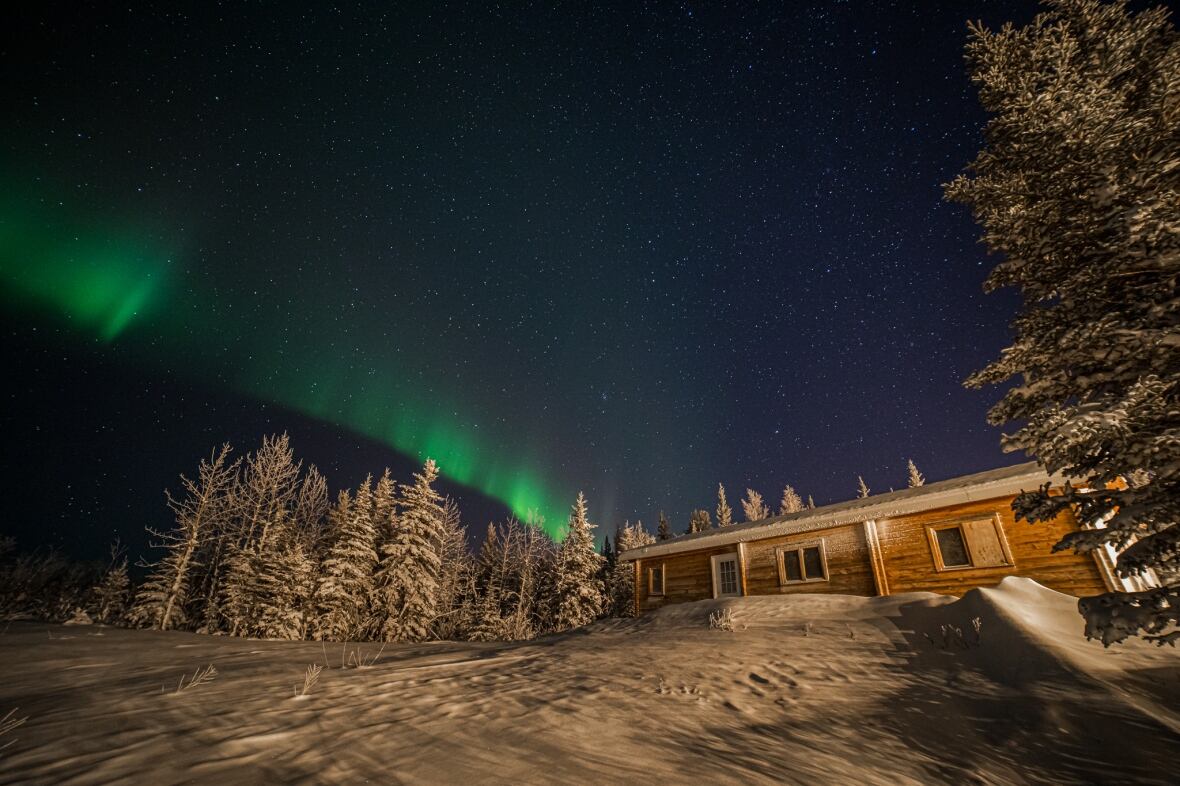 Northern lights seen above a cabin in the snowy woods.