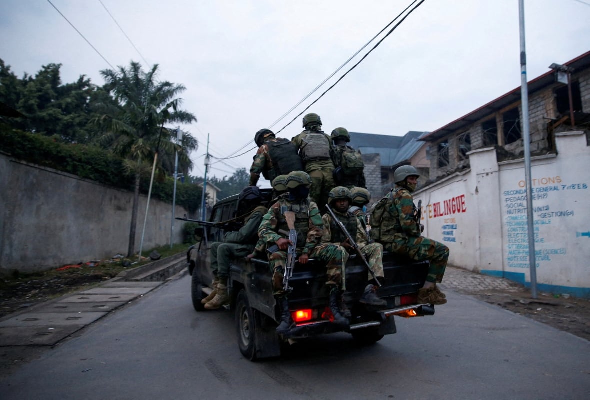 A group of armed rebels ride in a truck dressed in camouflage.