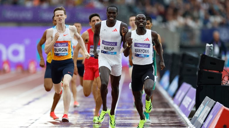 A group of men's athletes run in a small group on a track.