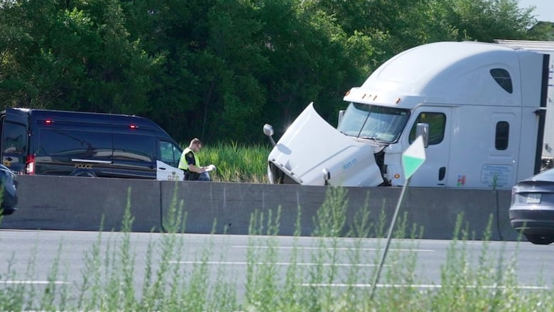 Photo showing a white tractor trailer with a damaged bumper opposite an Ontario Provincial Police vehicle on the highway.
