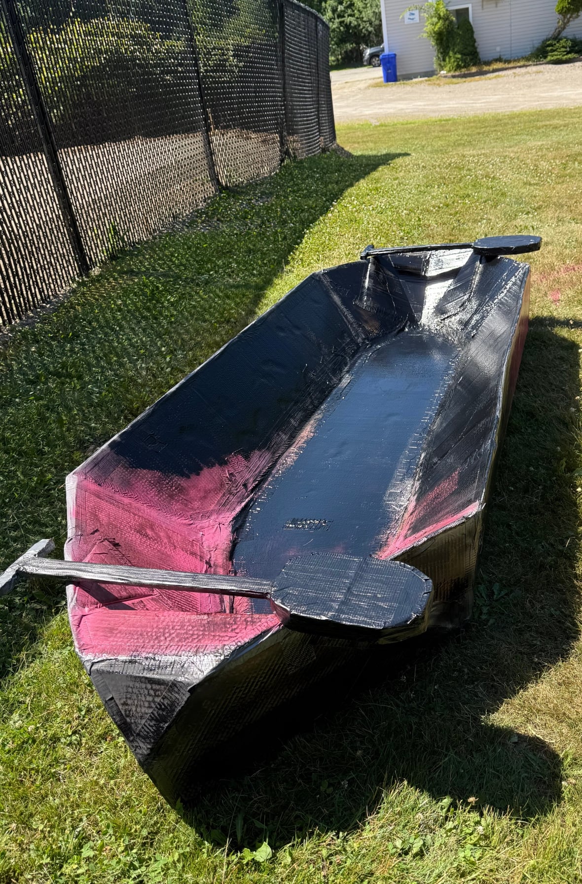 A black and pink cardboard boat with two cardboard paddles.