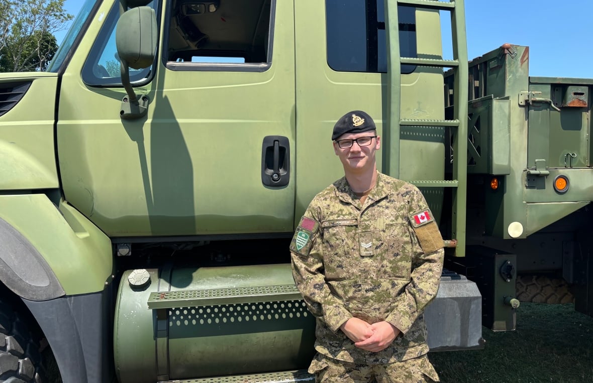A solider stands on the right side of a green military truck.