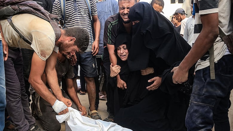 People embrace as they grieve over a body bag.
