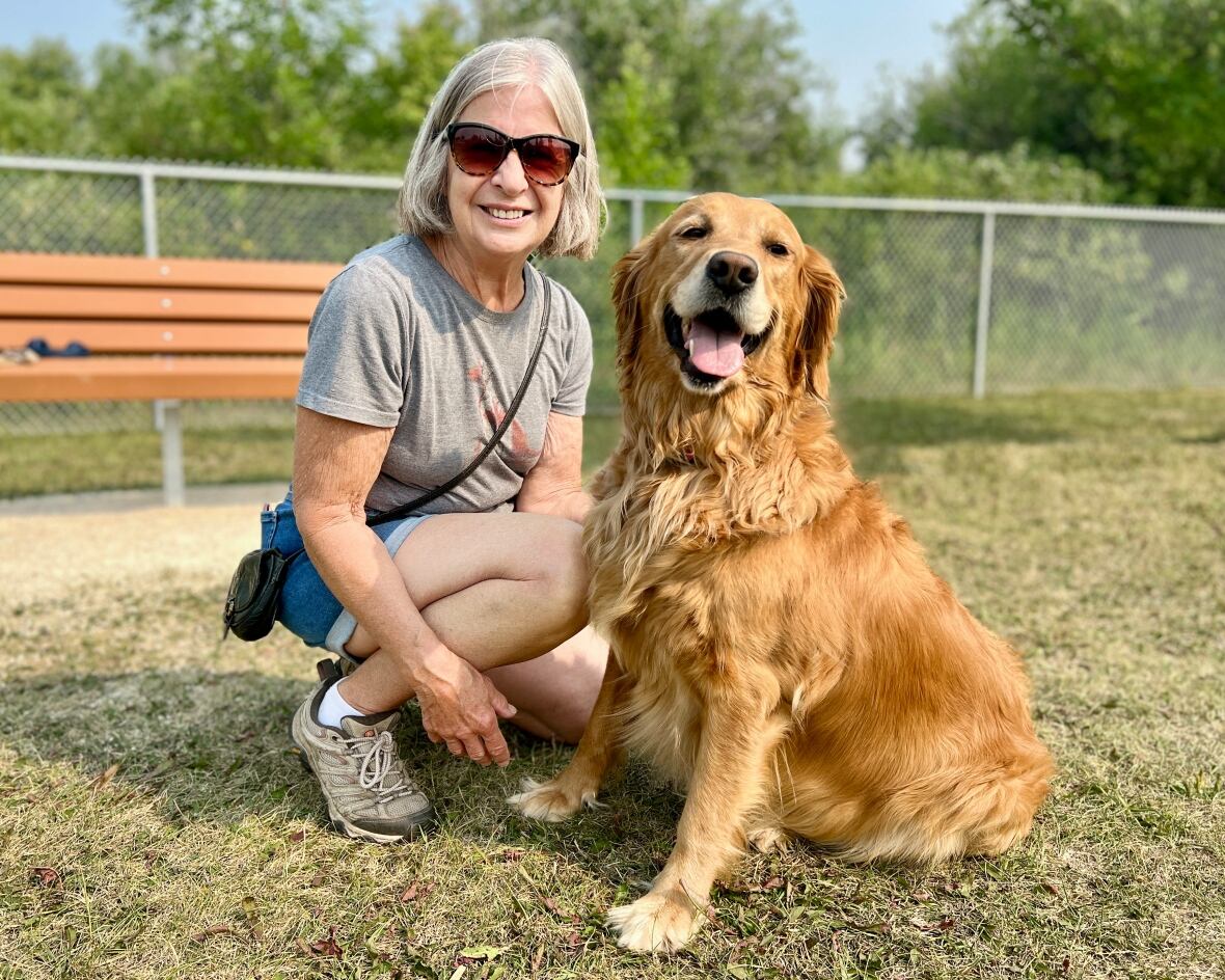 A woman poses with her brown dog for a picture in a field.