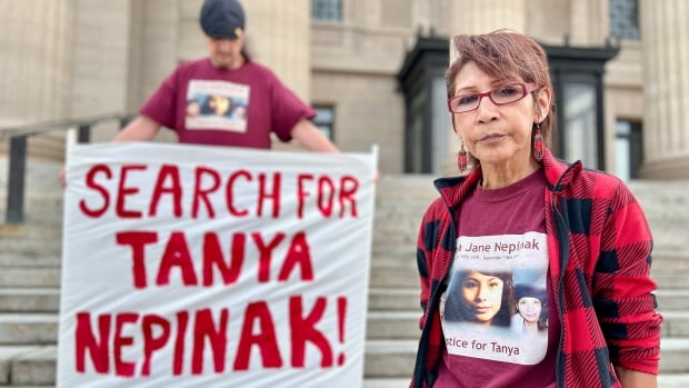 A woman stands at the bottom of large concrete steps and next to a person holding a sign that reads, 'Search for Tanya Nepinak.'