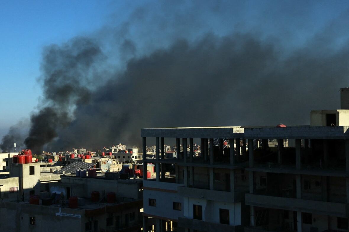 A large black plume of smoke rises above a city.