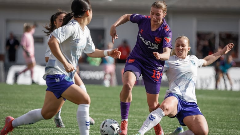 A female soccer player runs with the ball as an opponent slides to kick it away from her.
