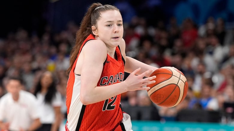 A female basketball player representing Canada dribbles the ball with her left hand.