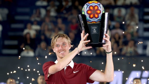 A male tennis player smiles while hoisting a trophy.