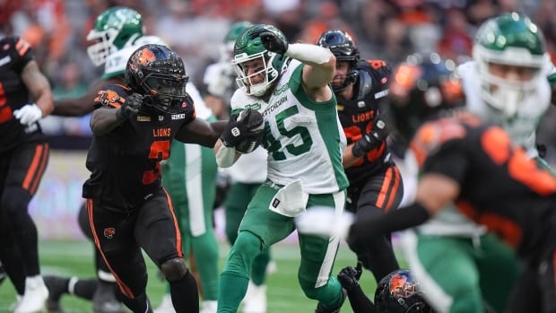 Football player in white and green holding a football runs past an opposing player in black and orange.
