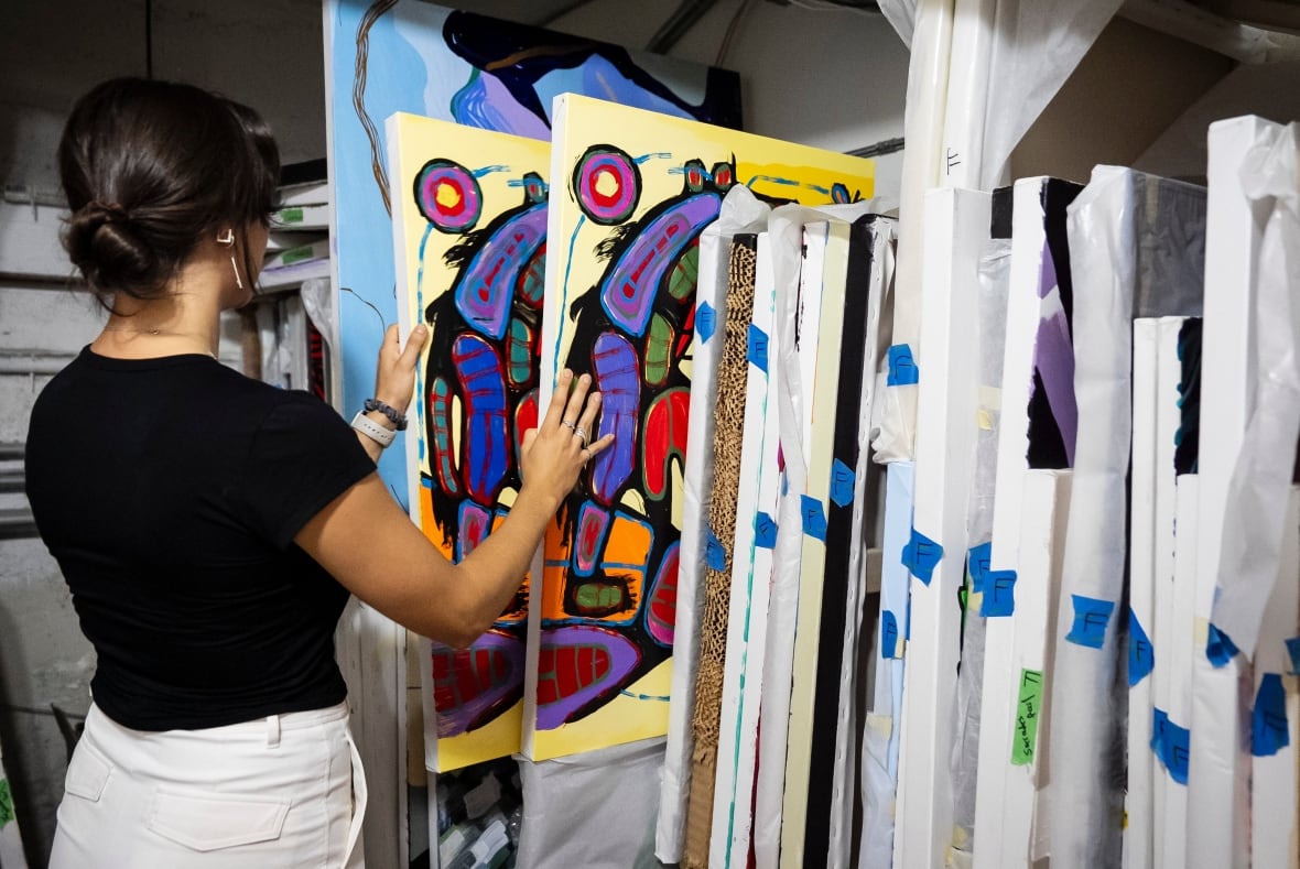 A woman browses through a rack of paintings.