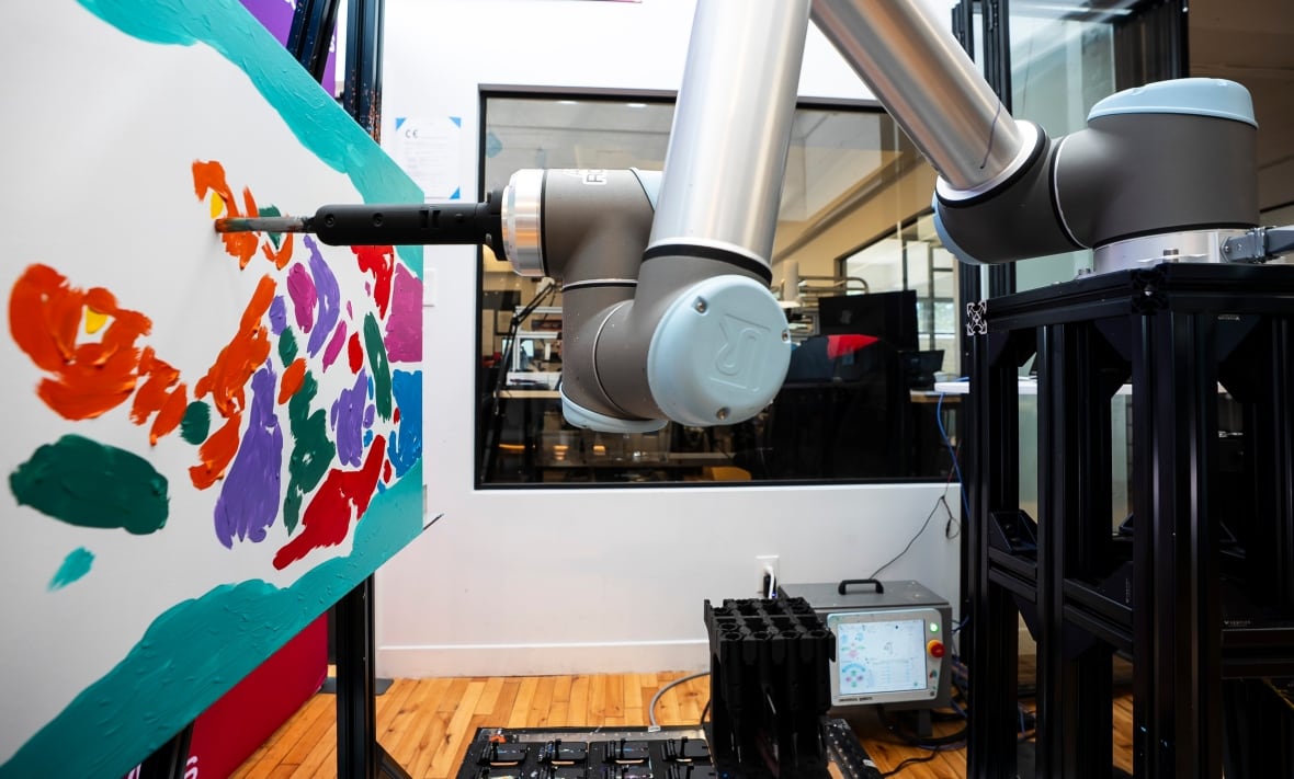 A robotic arms uses a brush to paint on a canvas.