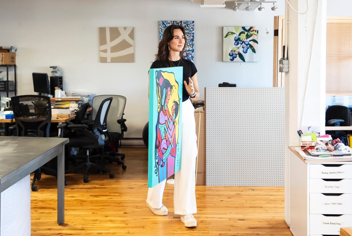 A woman holds up a painting.