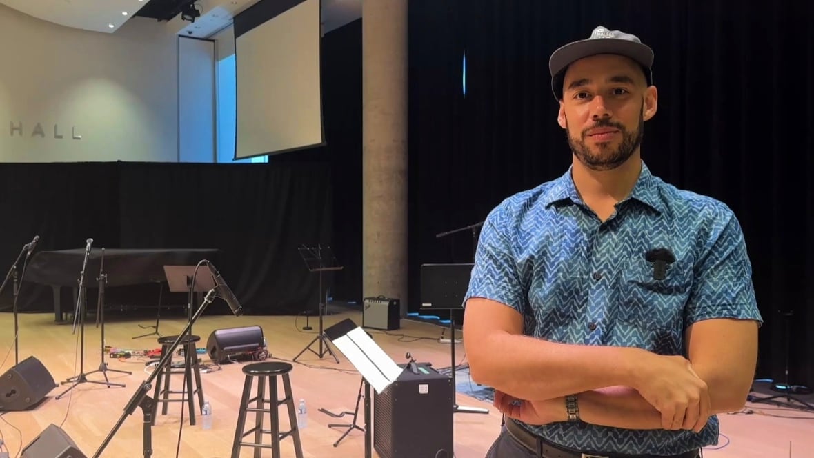 Andrew stands in front of several instruments on the stage at the Halifax Central Libary.
