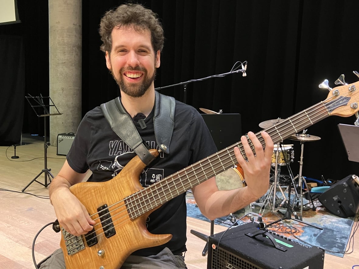 Carl sits on a stool holding his bass in his hands. 