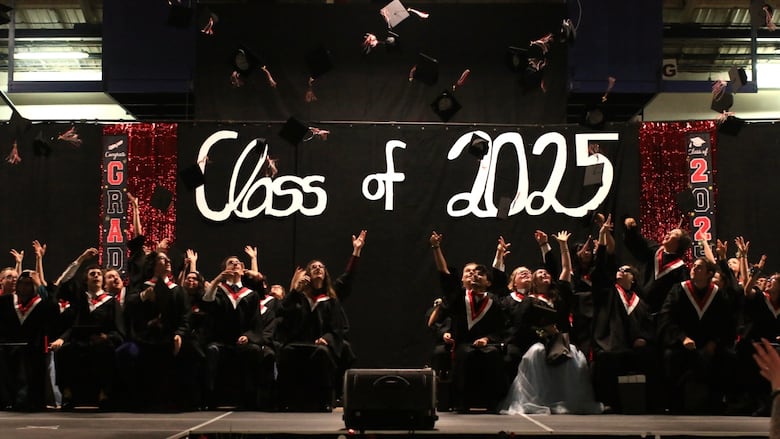 Graduates are seen throwing their caps into the air.