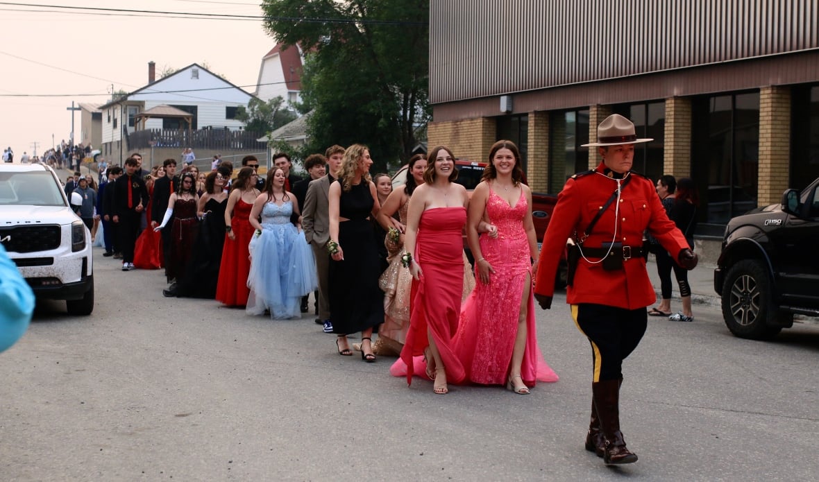 A lineup of grads in their dresses and suits walk down a street.