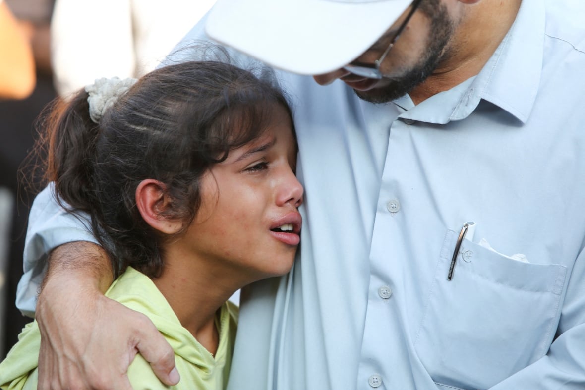 A child cries as she is held by a man.