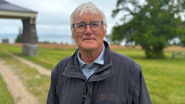A man in a black coat and white hair, smiles.