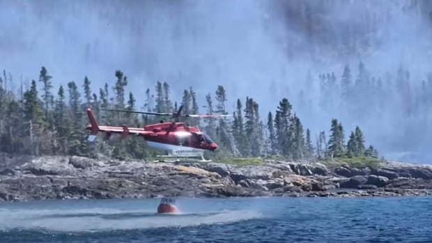 A helicopter near water getting a bucket of water.