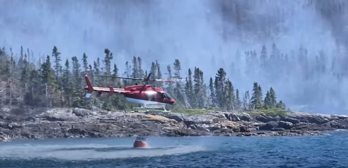 A helicopter near water getting a bucket of water.