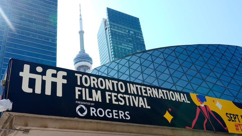 An exterior shot of a banner on top of a building, reading "TIFF" and "Toronto International Film Festival." The CN Tower and other skyscrapers are in the background.