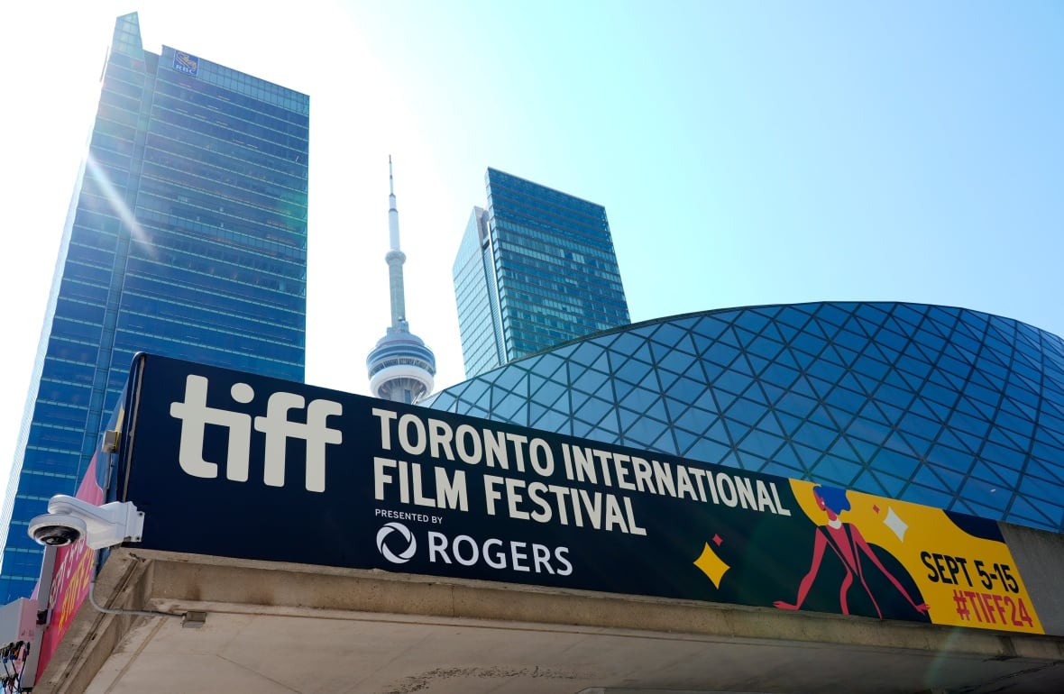 An exterior shot of a banner on top of a building, reading "TIFF" and "Toronto International Film Festival." The CN Tower and other skyscrapers are in the background.