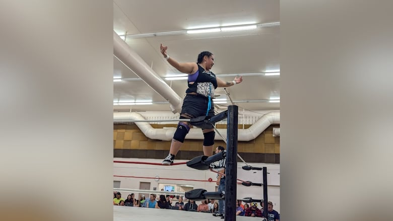 A teenage girl standing in a wrestling ring with her arms up.