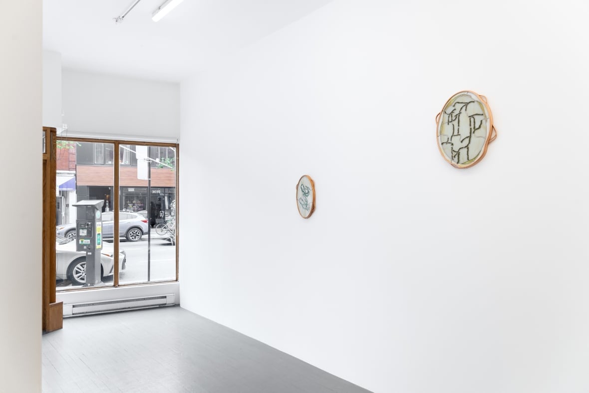 On one wall of a white exhibition space hang two stained glass artworks framed in copper hoops.