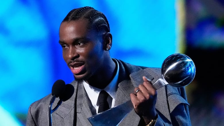 A person in a suit holding a trophy speaks into a microphone.