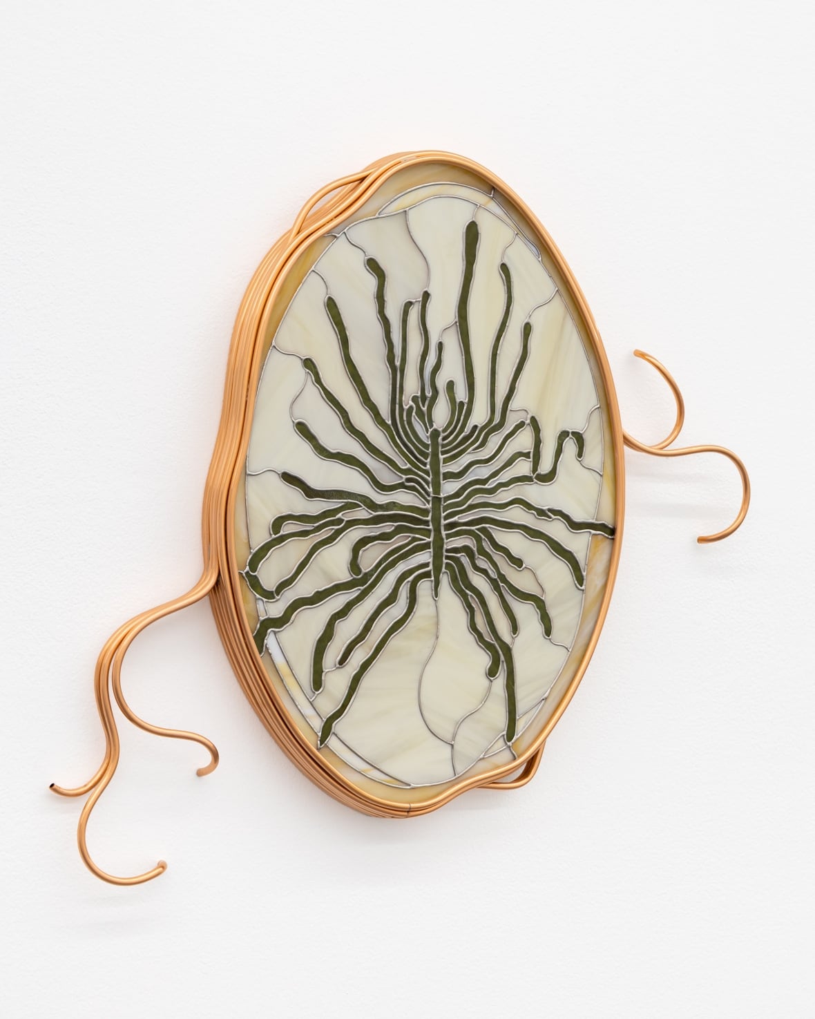 Hanging in an ornate copper frame, a cream-coloured stained glass artwork is marked by radiating green lines.