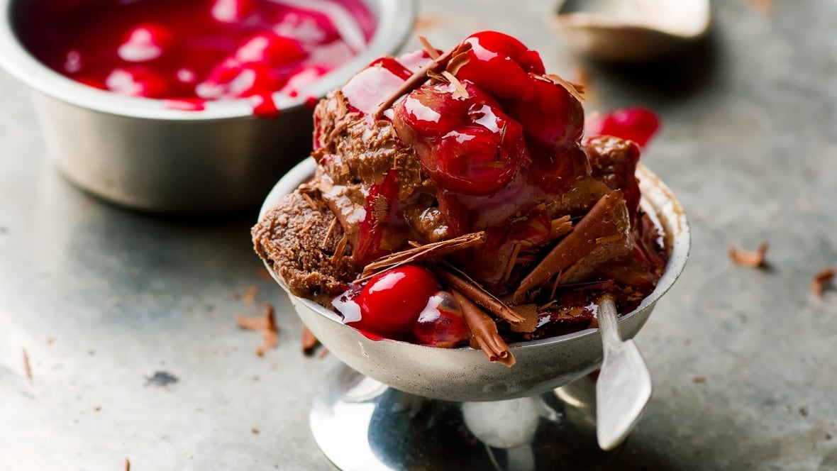 Closeup on chocolate ice cream topped with cherry preserves in a silver dish.