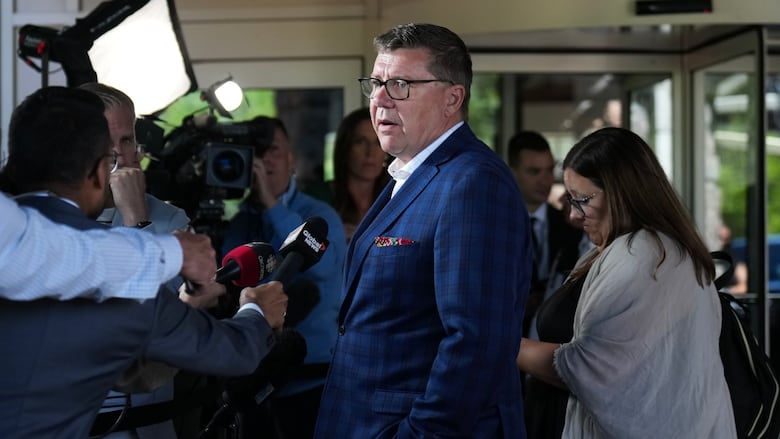 A man in a suit speaks to reporters.
