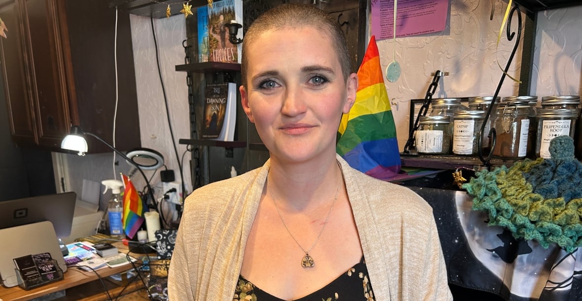 A woman with a tan jacket stands in front in a office.