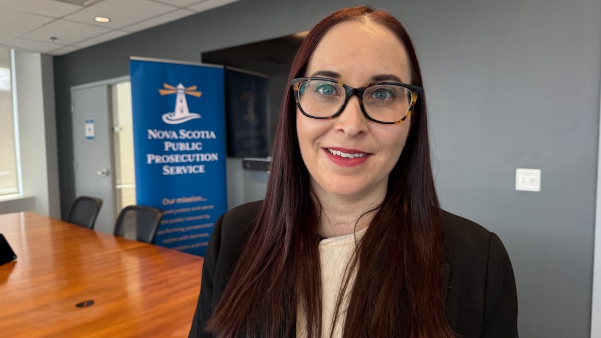 A portrait of a woman wearing glasses standing in a boardroom.