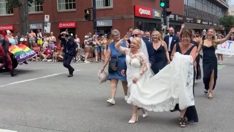Woman in wedding dress at a street corner during a parade