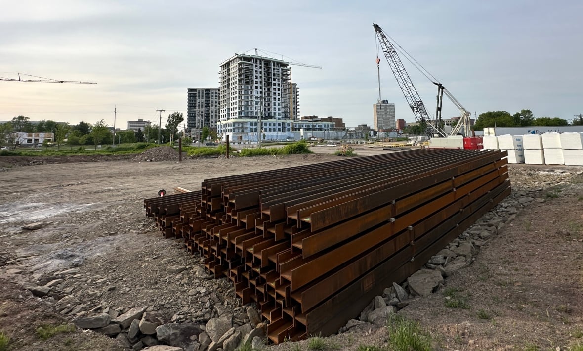 A pile of steel at the construction site where two downtown towers are planned with construction underway on other towers in the background.