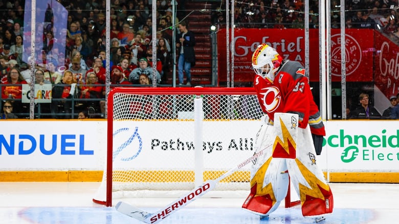 A goaltender looks down as she stands in her crease.