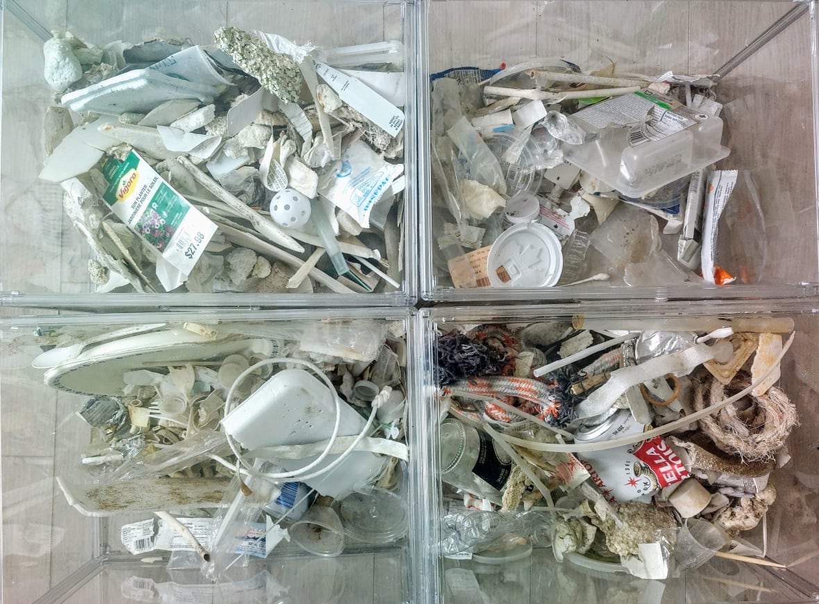 Top down view of four clear bins filled with white-coloured trash. Items include beer cans, coffee cup lids, phone chargers, styrofoam, plastic cutlery and wiffle balls.
