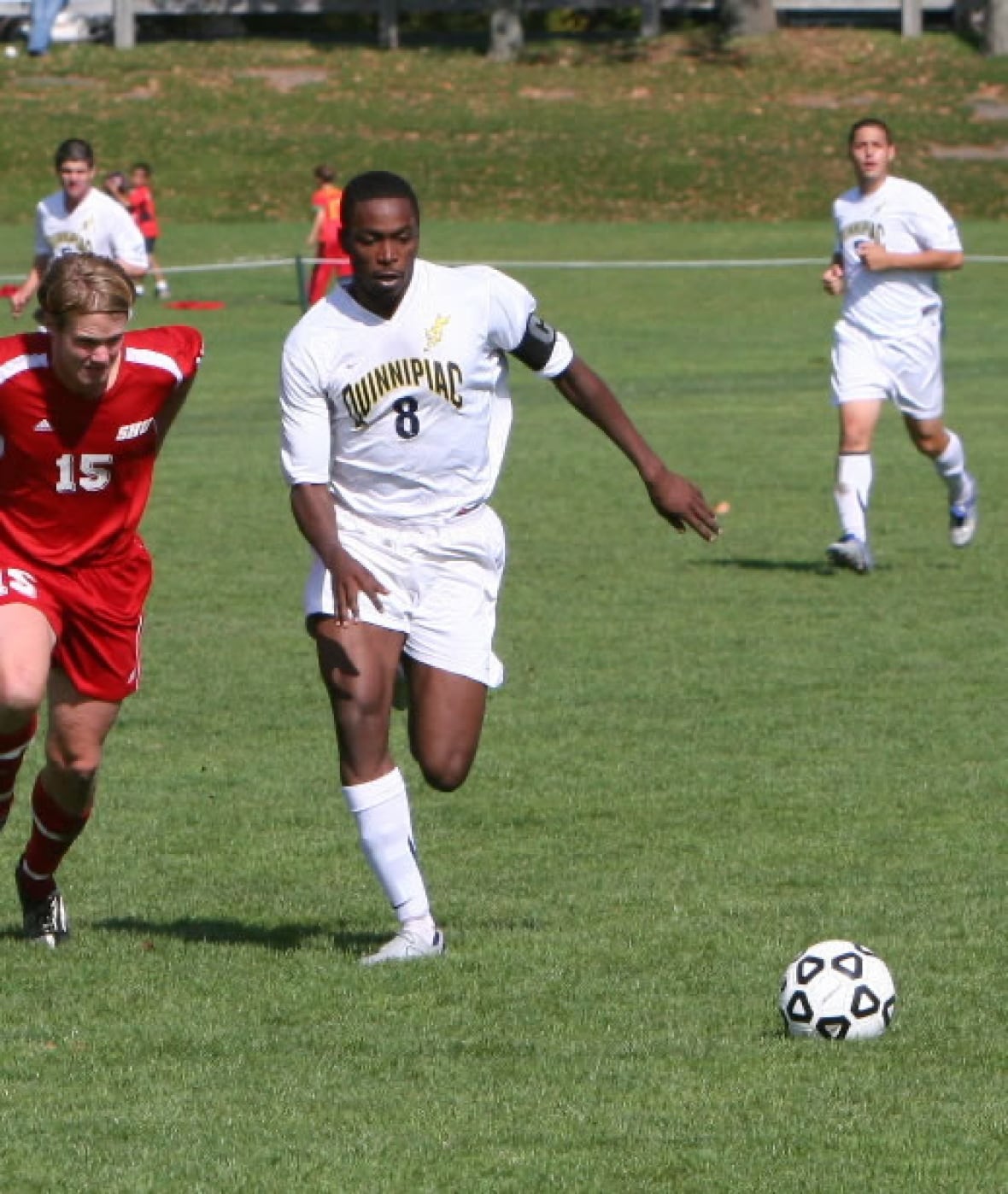 A man in a white uniform runs after a soccer ball.